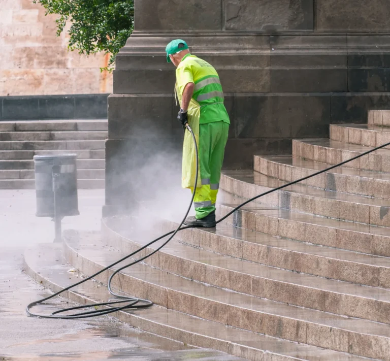 Worker in green high visibility gear pressure washing stone steps